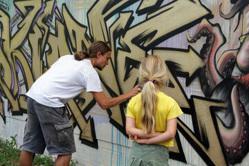 Blondes Mädchen schaut Graffiti Sprüher an der Wand zu - 468357884