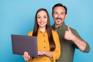 Photo of brunette haired husband wife couple hold laptop make thumb up isolated on blue color...