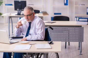 Old male employee in wheel-chair drinking coffee during break