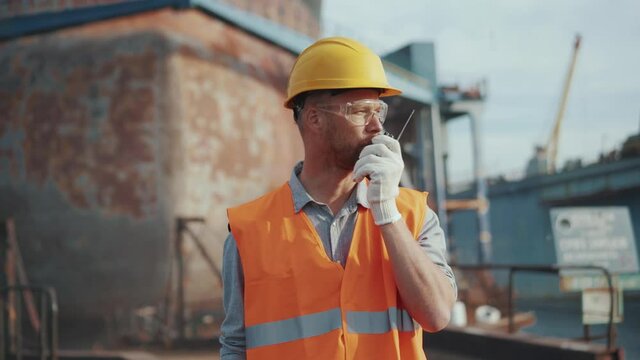 Confident man shipbuilder in uniform talking into walkie-talkie outdoors