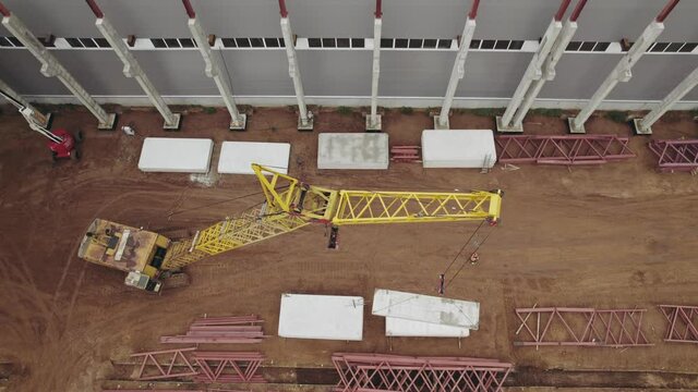 Aerial view. A heavy crane at a construction site is lifting iron concrete slabs.
