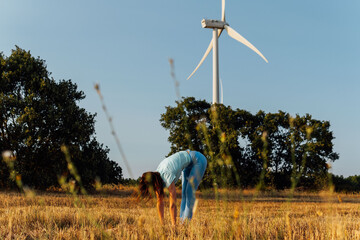 beautiful middle aged young woman doing stretching in cereal field with windmills in the background