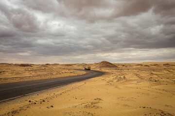 Fototapeta na wymiar A truck drives along a road leading through the Black and White Desert in Bahariya. Egypt