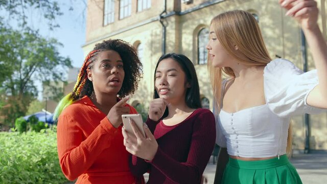 Group of female students using maps app in smartphone, travelling together