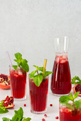 Refreshing pomegranate juice in glasses with mint and glass straw, pitcher of juice and ice, cold drink