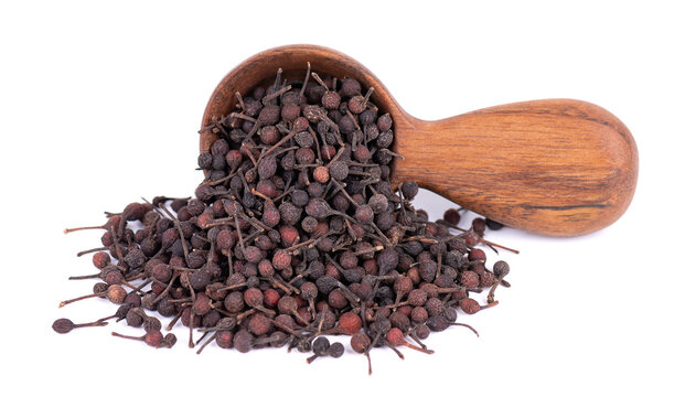 Bourbon pepper in wooden spoon, isolated on white background. Voatsiperifery or bourbonese piper. Madagascar pepper.