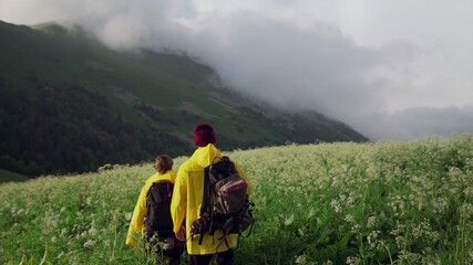 Young woman and man tourists in yellow raincoats walk through the mountainous areas and look at the beautiful nature. Tourism
