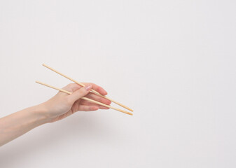 Female hand with japanese wooden chopsticks close up on white background