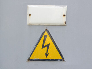Yellow sign warns of high voltage on an old gray metal door close-up