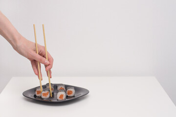 Female hand with chopsticks takes a Philadelphia roll with black plate on a white background