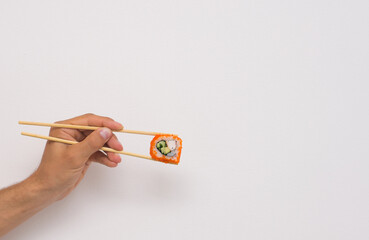 Male hand holding chopsticks roll close up on white background