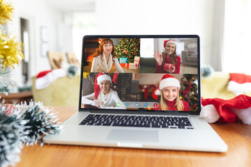 Four smiling caucasian women in santa hats on laptop christmas group video call interface screen