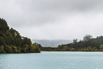 Lake between mountains with forest to the shore on a foggy day