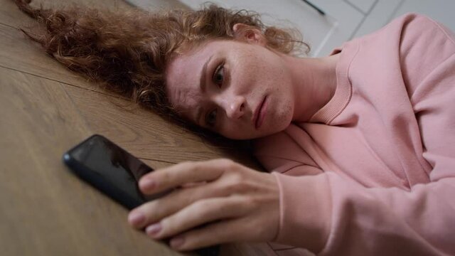 Sad young caucasian woman lying on floor and checking mobile phone. Shot with RED helium camera in 8K.