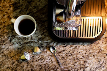 Cup of coffee, coffee machine and capsules on marble kitchen countertop. Home cafe concept.