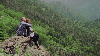 A young man and a girl are sitting on a rock in a mountainous area and looking at beautiful landscapes. Tourism