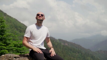 A young man in sunglasses, sitting on a rock and enjoying life. Tourism and travel