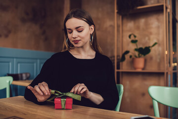 Young woman opening gift while having rest in coffee house