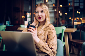 Thoughtful young woman with takeaway coffee and laptop in cafe alone