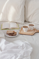 Breakfast on dark wooden vintage tray in bed with light beige sheet and pillows. Flat lay, top view. Slow romantic morning concept.