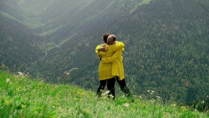 Naklejka premium A young woman in a yellow raincoat is a young couple hugging in a mountainous area. Travel and tourism