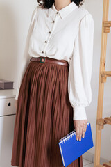 Young pretty woman in pleated skirt, white shirt holding a notebook on white background. Fashion vintage inspired clothes look.