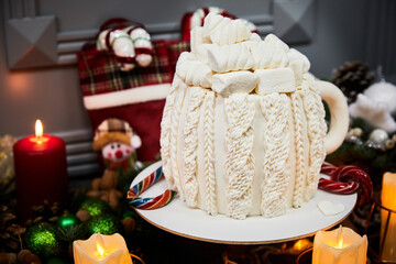 Christmas cake with wet chocolate base, cream cheese, salted caramel and nuts on the background of candles, garlands, fir branches and cones