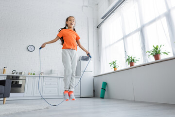 Low angle view of kid jumping with skipping rope in kitchen - obrazy, fototapety, plakaty