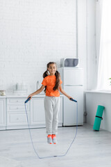 Smiling girl jumping with rope in kitchen at home - obrazy, fototapety, plakaty