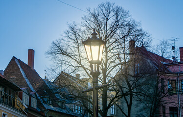 A medieval-style lantern on the street of the old town with sunlight shining through it against the background of the blue sky and houses. shining lantern