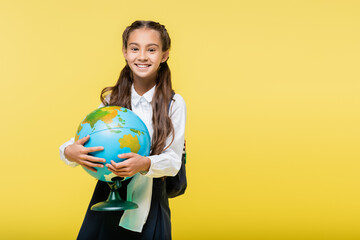 Happy schoolgirl holding globe and looking at camera isolated on yellow