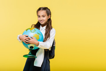 Schoolkid holding globe and smiling at camera isolated on yellow