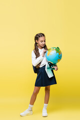 Fototapeta premium Positive schoolchild with backpack looking at globe on yellow background