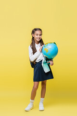 Smiling schoolgirl holding globe on yellow background