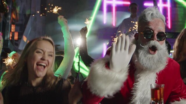 Stylish modern Santa Claus drinks alcohol with beautiful smiling girls in bar.