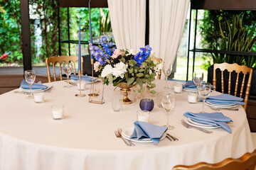 Festive wedding, table setting with blue linen napkins, candles and fresh flower bouquets. Wedding decorations. Restaurant menu concept. Soft selective focus.