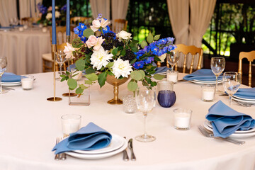 Festive wedding, table setting with blue linen napkins, candles and fresh flower bouquets. Wedding decorations. Restaurant menu concept. Soft selective focus.