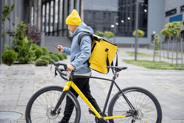Courier with bicycle searching client's place with GPS on smartphone in city. Concept of shipping and logistics during Coronavirus pandemic. Idea of profession and job. Asian man wearing warm clothes