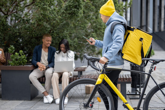 Courier walking with bicycle on background of working business people in city. Concept of shipping and logistics. Remote and freelance business work. Businessman and businesswoman talk and use laptop