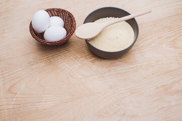 dark stoneware bowl with flour and white eggs on a rustic wooden tabletop