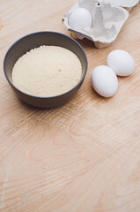 dark gray bowl with whole wheat flour and white eggs on a rustic wooden tabletop