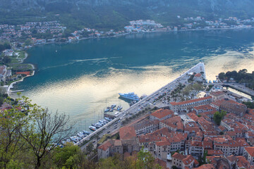 A view from above of the bay with yachts and boats and houses with red tiled roofs. Sunset time. The concept of tourism in Montenegro.