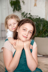 Older and younger sisters hugging in   home interior.