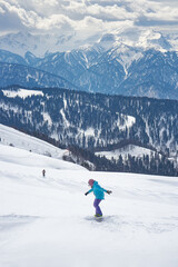 Snowboarder girl starting the ride on the background of the panorama of Caucasus mountain ridge in Krasnaya Polyana (Sochi, Russia)