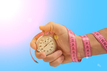 Stopwatch in hand wrapped with measuring tape, on blue background with bright sun.Fitness sports...