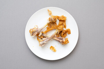 Messy food leftover, chicken bones as fast food on the ceramic white plate, top view