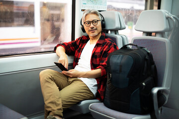 Senior man traveling by train. Man listening the music while enjoying in travel.
