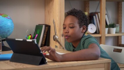 Online education at home. Happy African-American schoolboy does test spbd on tablet sitting at table with copybook and globe close side view - Powered by Adobe