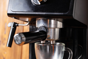 Making coffee in a coffee machine in the kitchen, close-up. Black coffee flowing into a transparent cup on a wooden table top background