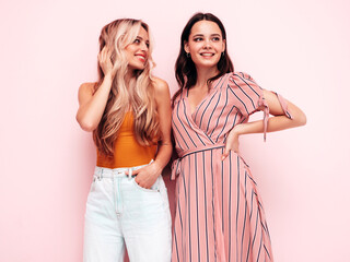 Two young beautiful smiling brunette hipster female in trendy summer clothes. Sexy carefree women posing near pink wall. Positive models having fun. Cheerful and happy